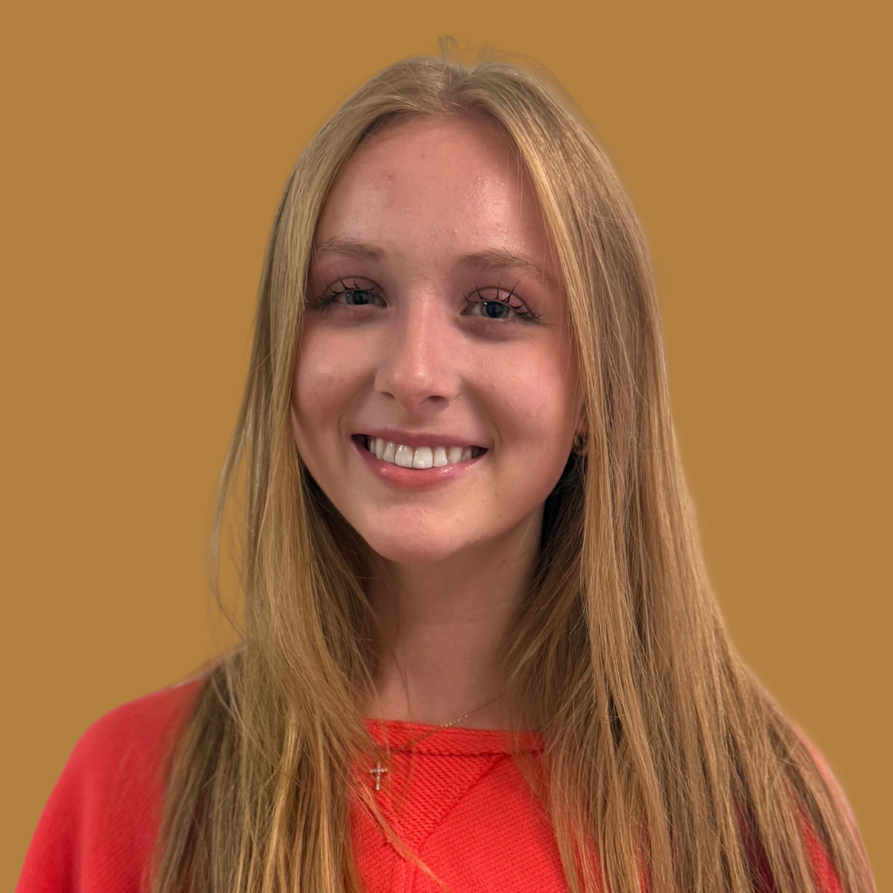 Blonde woman with long hair wearing a red shirt stands against a yellow background, smiling.