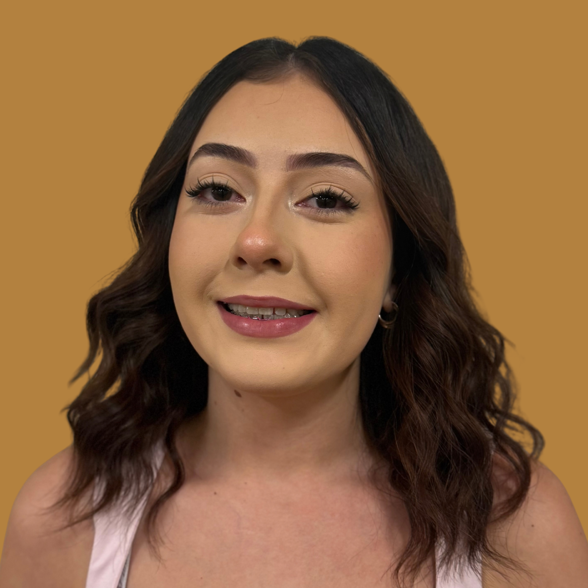 A smiling person with curly hair and braces. They wear a white sleeveless top. The background is plain orange.