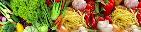 A vibrant display of various fresh vegetables, including leafy greens, peppers, garlic, and carrots, arranged side by side.