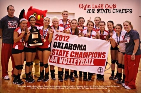 A group of female volleyball players, along with their coach, celebrate their victory as the 2012 Oklahoma State Champions in 4A Volleyball, holding a large banner that reads '2012 Oklahoma State Champions 4A Volleyball.'
