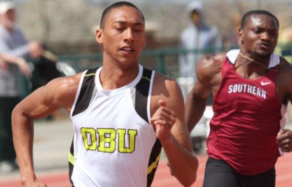 Two male athletes are competing in a sprint race on an outdoor track, with one wearing a white jersey with 'DBU' and the other in a maroon jersey with 'SOUTHERN'.