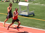 Two male athletes are competing in a sprint race on a track, with one runner in a red uniform leading and another in a black uniform closely behind.