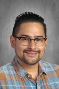 A smiling man wearing glasses and a plaid shirt, exuding a friendly and approachable demeanor.