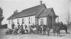 A diverse group of individuals gathered outside a school building, engaged in conversation and enjoying the day.
