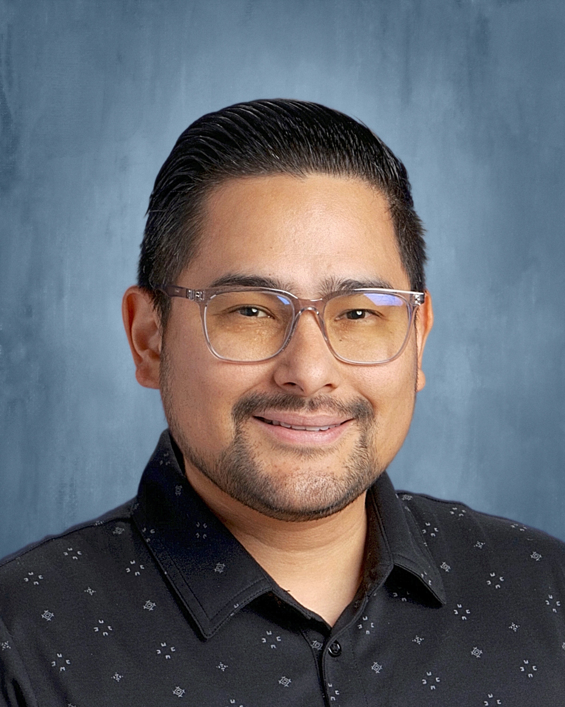 A smiling man wearing glasses and a plaid shirt, exuding a friendly and approachable demeanor.