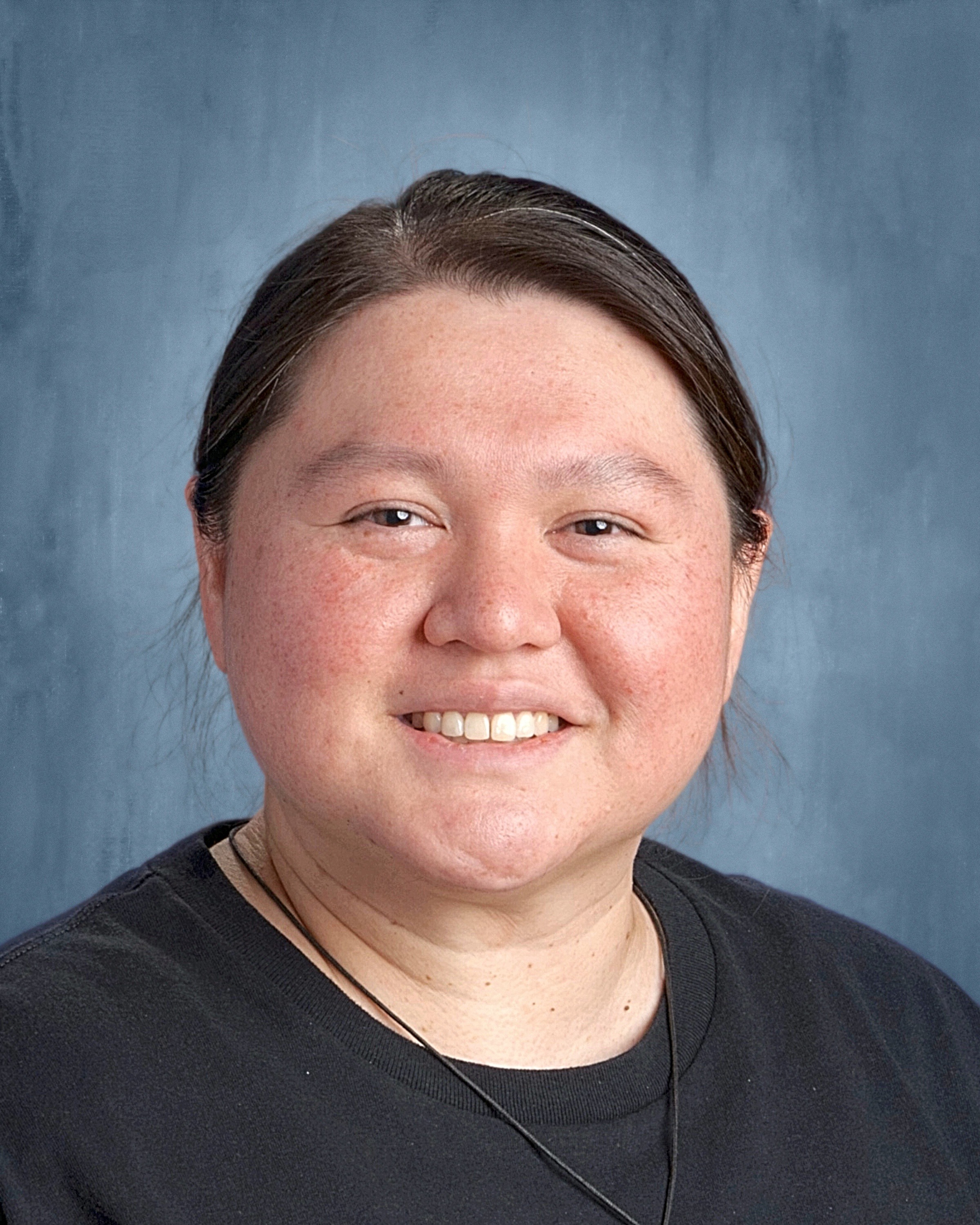 A woman wearing a black shirt smiles warmly at the camera, exuding confidence and joy.