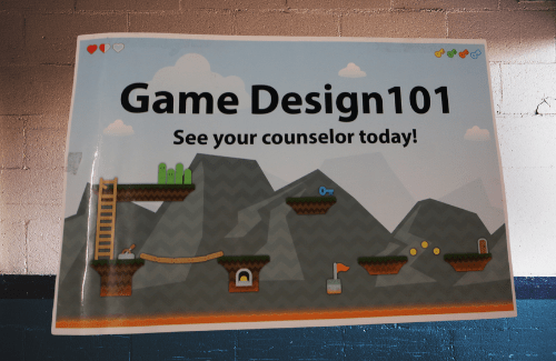 A colorful poster promoting a course titled 'Game Design 101,' featuring stylized mountains and game elements, with a message encouraging viewers to see their counselor today.