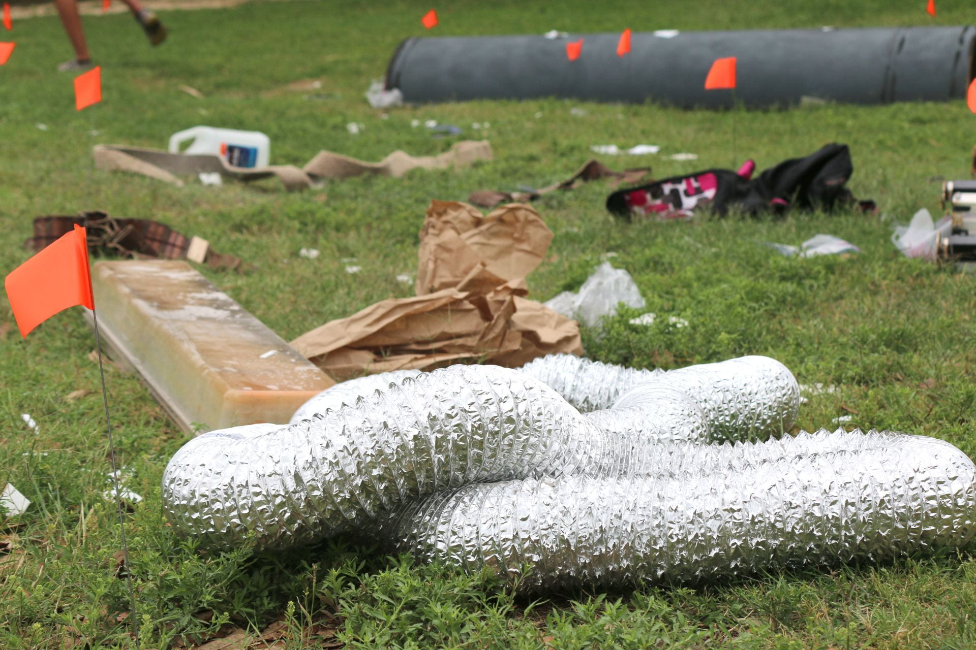 A partially covered area of grass littered with various items, including a shiny, silver, inflatable figure, cardboard, and other debris.