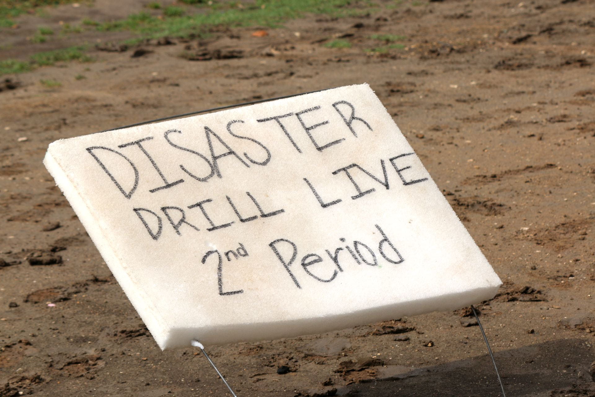A sign on the ground reads 'DISASTER DRILL LIVE 2nd Period' in bold black letters on a white background, indicating an ongoing emergency drill.