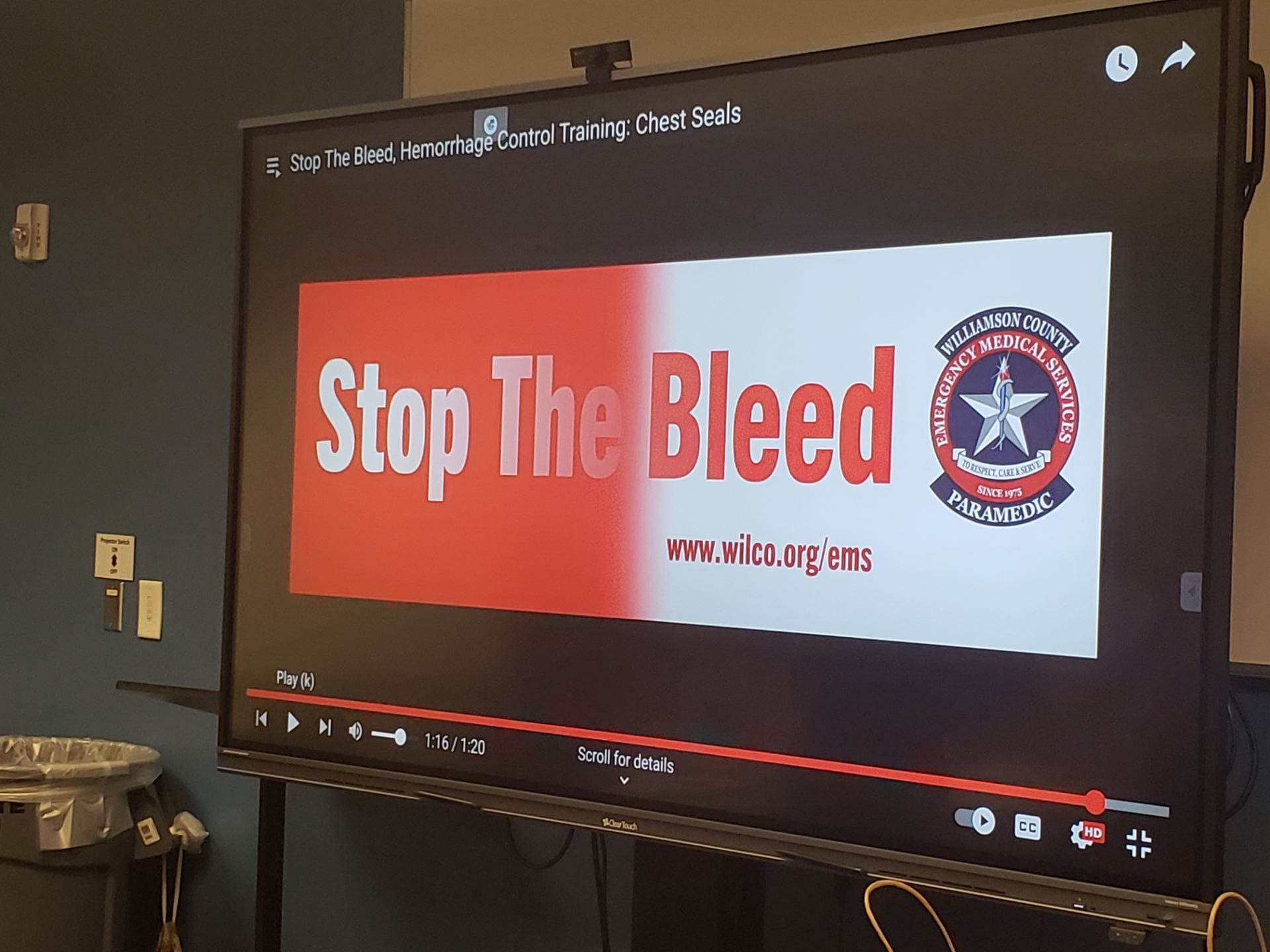 A digital screen displaying a presentation slide with the text 'Stop The Bleed' and a logo, set in a training environment.