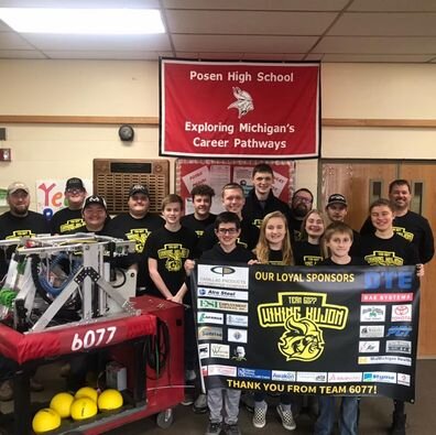A team stands proudly with their robot and a banner, showcasing their achievement and teamwork in robotics.