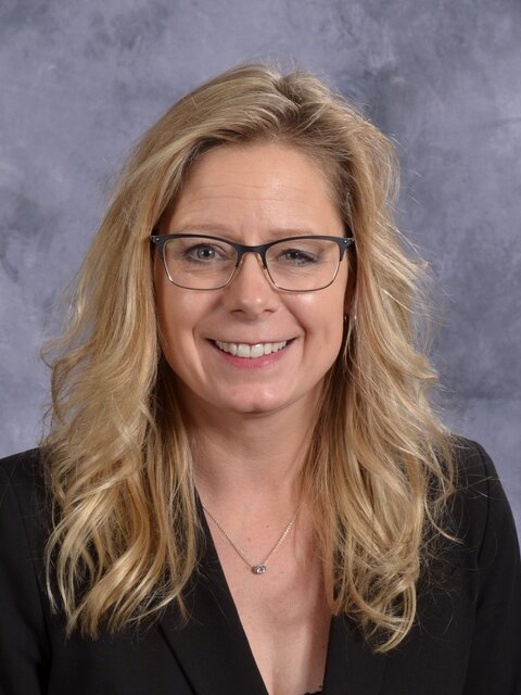 A woman wearing glasses and a black blazer, exuding professionalism and confidence in her appearance.