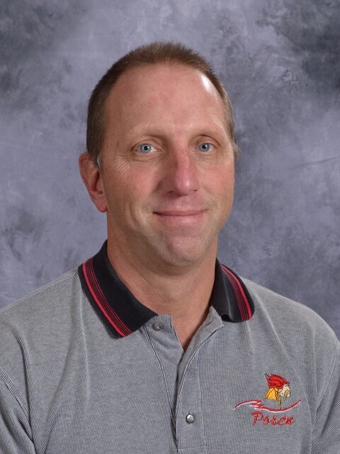 A man wearing a polo shirt and gray pants stands confidently, showcasing a casual yet polished appearance.