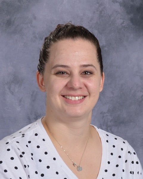 A woman wearing a polka dot shirt smiles warmly, radiating joy and positivity in her expression.