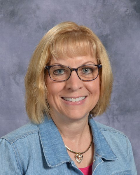 A woman wearing glasses and a denim jacket, smiling confidently against a neutral background.