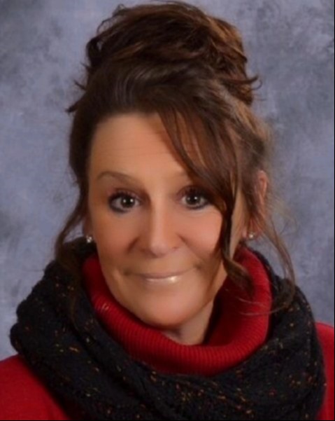 A woman wearing a red sweater and a black scarf, standing confidently with a warm smile.