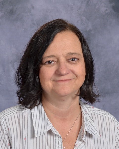 A woman with black hair wearing a striped shirt, standing confidently with a neutral background.