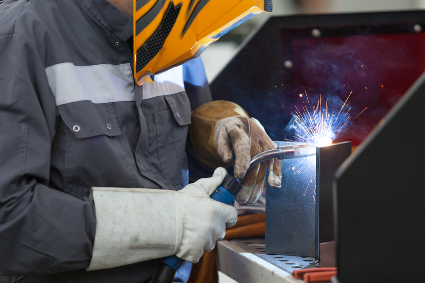 A welder in protective gear is working on a metal piece, with sparks flying from the welding process.