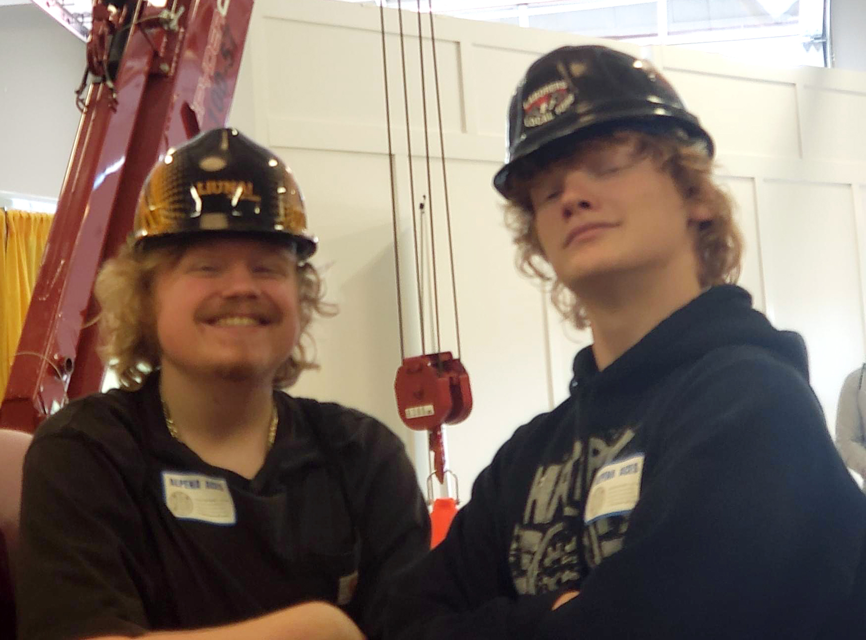 Two young men wearing hard hats pose confidently with arms crossed, smiling at the camera.