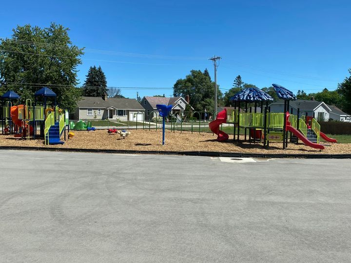 A colorful playground featuring slides, climbing structures, and swings, surrounded by grass and trees under a clear blue sky.