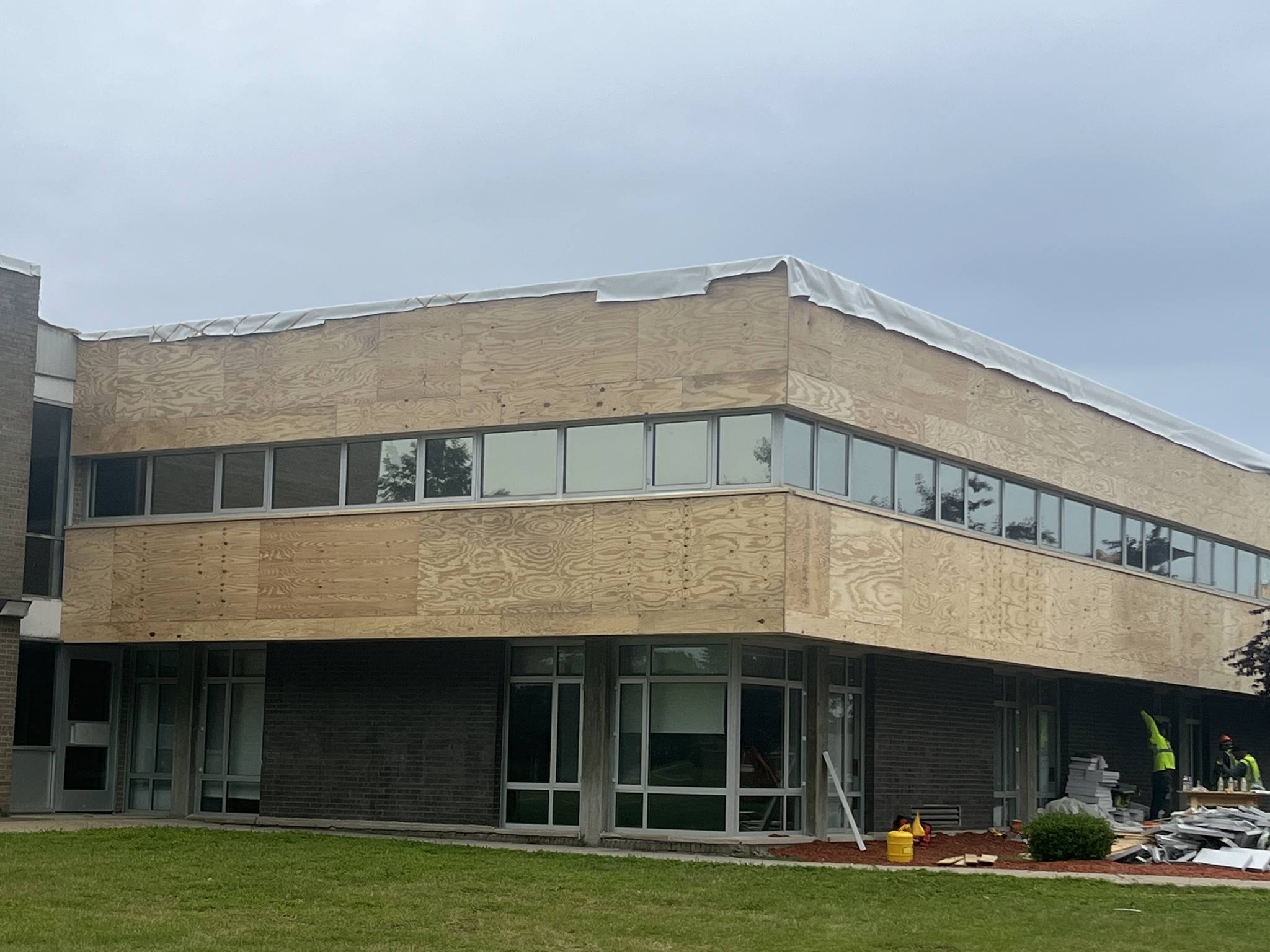 A modern building with a flat roof and large windows, featuring a mix of concrete and brick exterior, set against a cloudy sky.