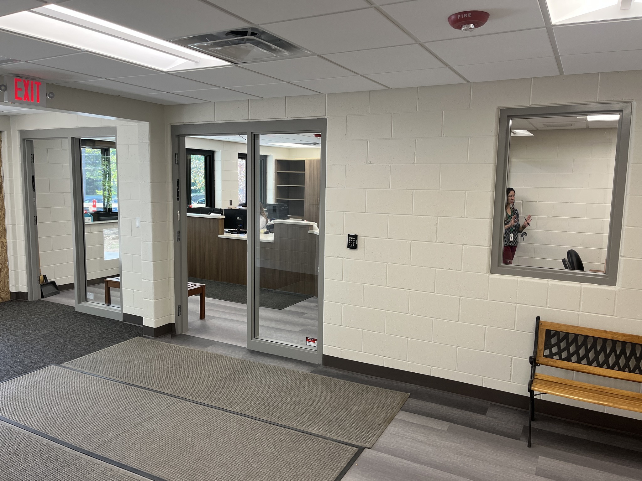 An interior view of a modern office lobby featuring glass doors leading to a reception area, a bench, and a mirror on the wall.