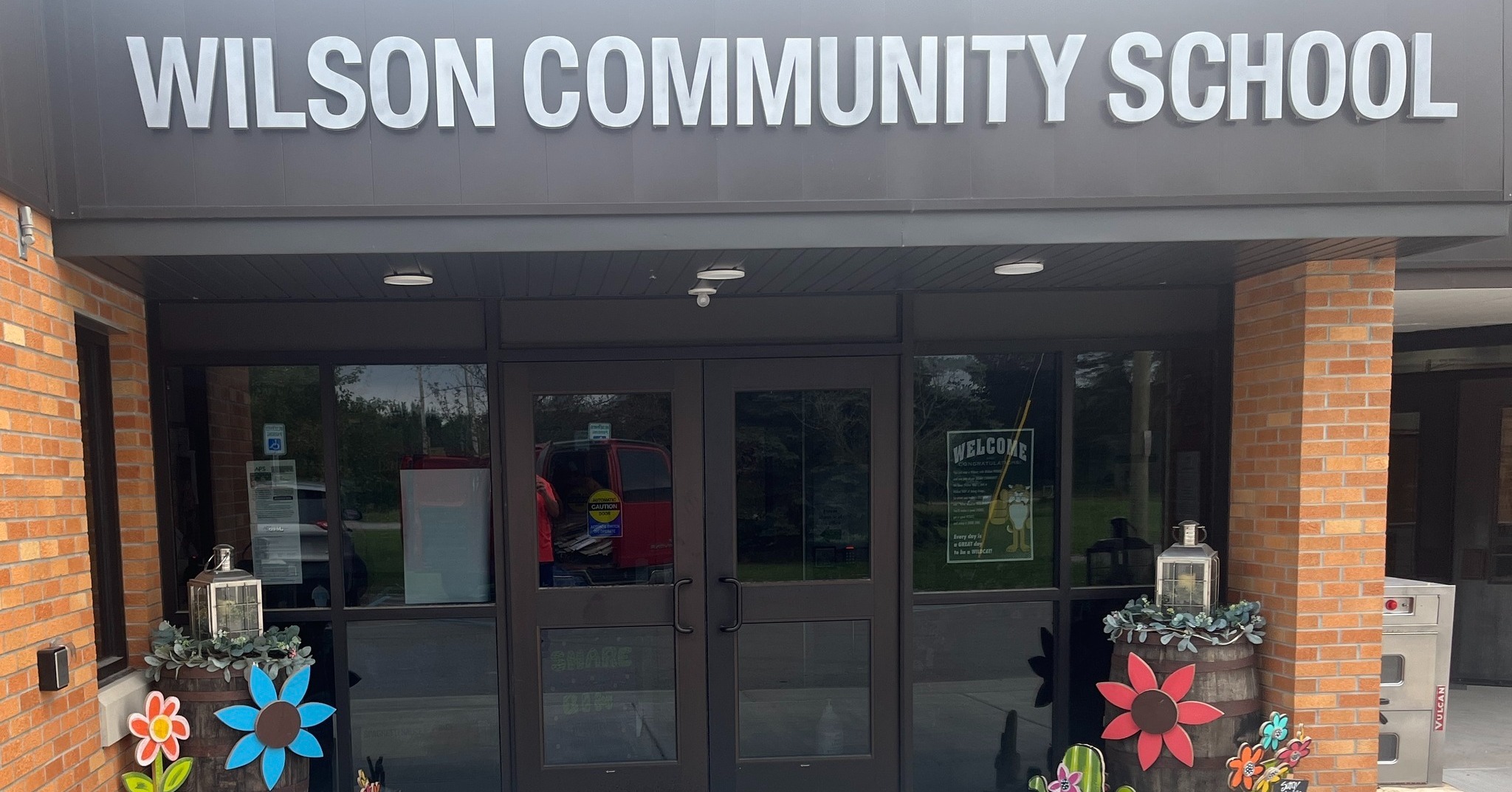 The entrance of Wilson Community School, featuring large glass doors and colorful flower decorations on either side.