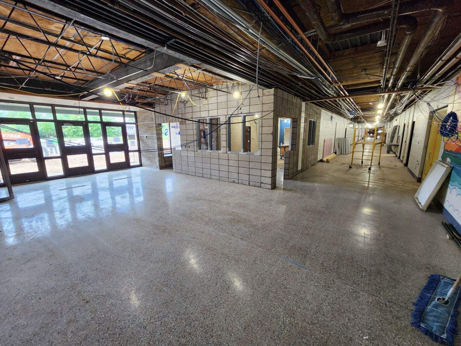 An interior view of a spacious, unfinished building with polished concrete floors, exposed ceiling beams, and large windows allowing natural light to enter.