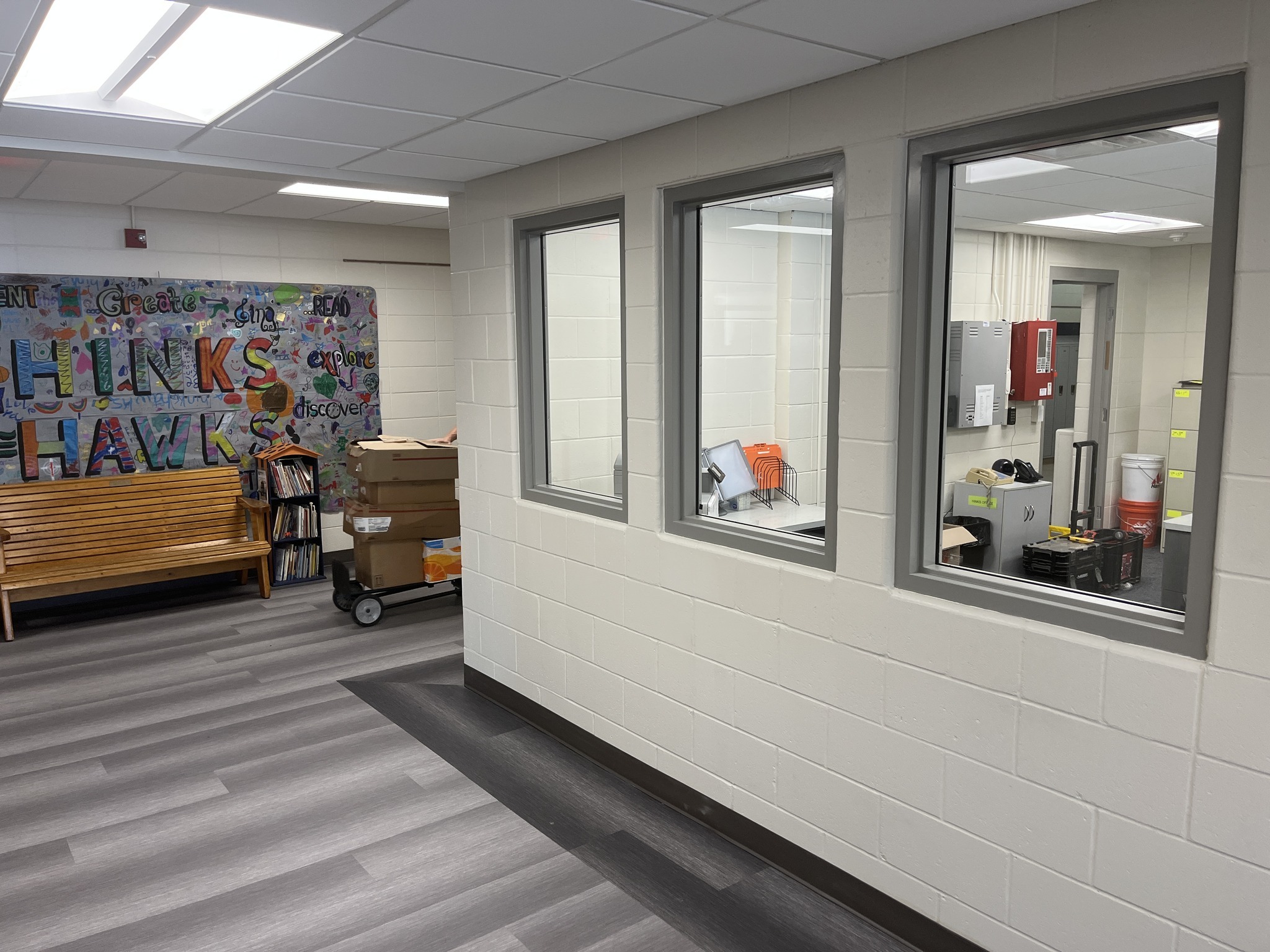 A view of a hallway featuring a colorful mural that says 'THINK HAWKS,' with a bench and windows leading to an office area.