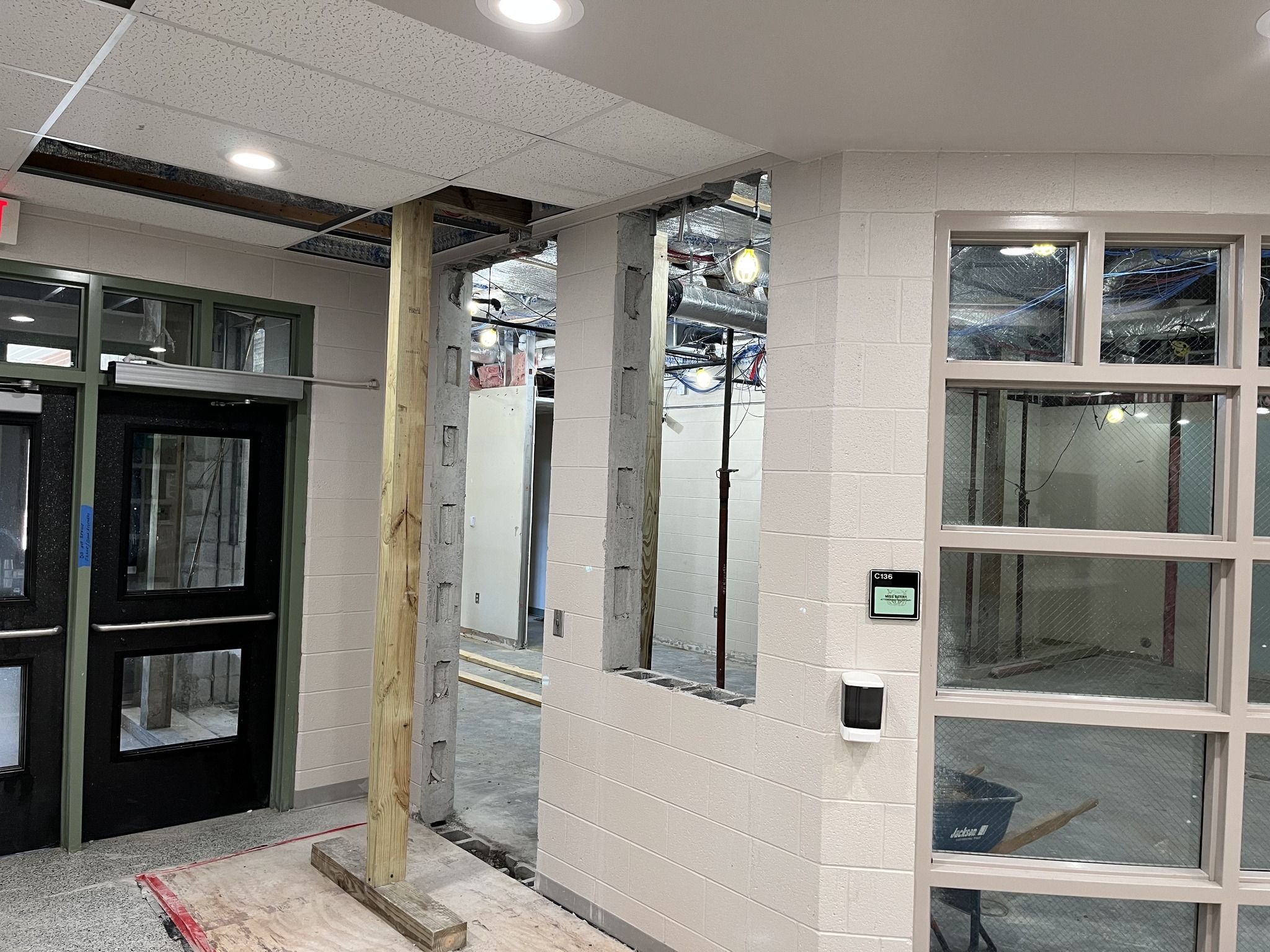 An interior construction site showing a partially finished room with exposed walls, a wooden support beam, and large glass windows on one side.