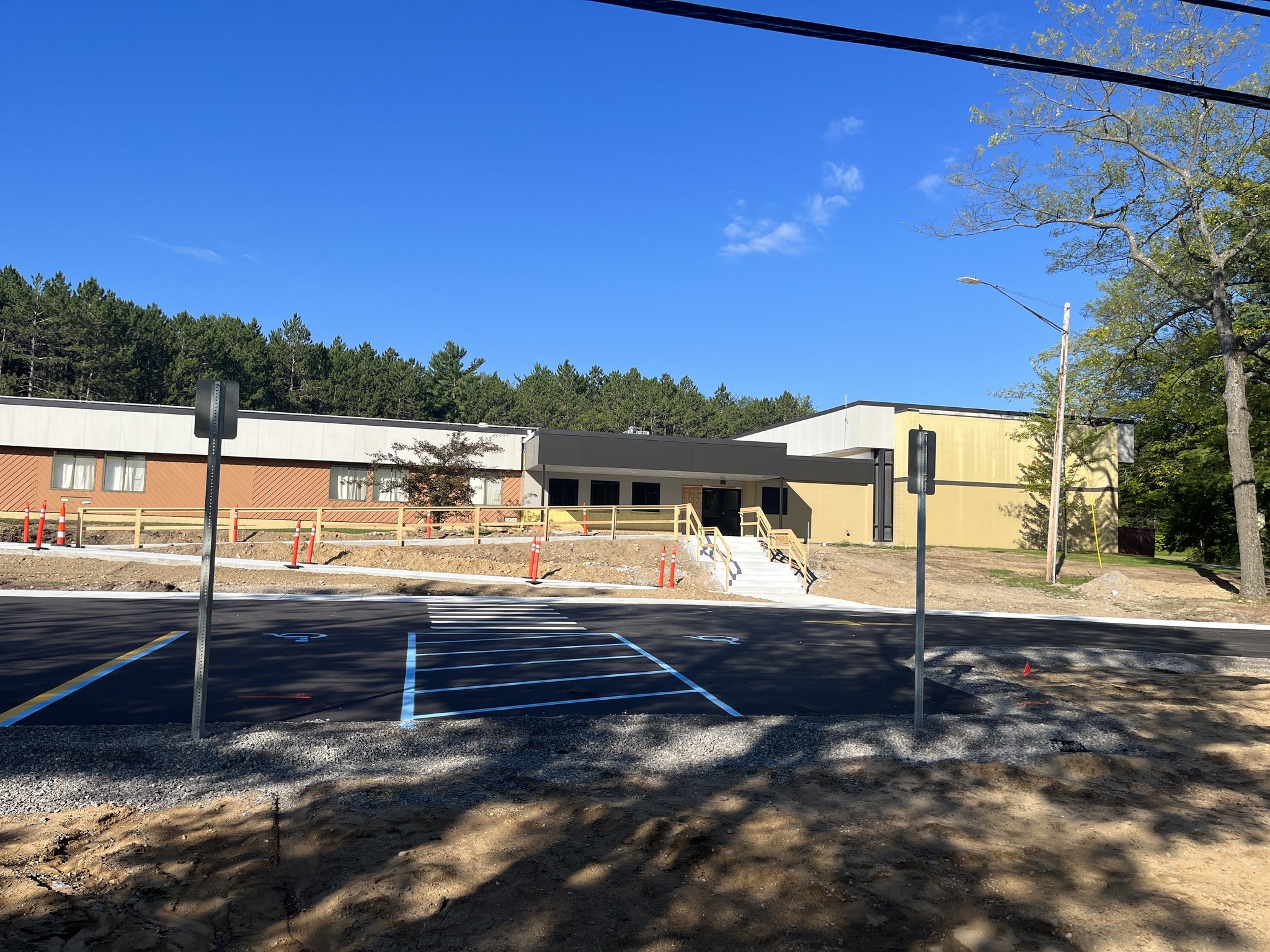A view of a newly constructed building with a parking area in the foreground, surrounded by trees under a clear blue sky.