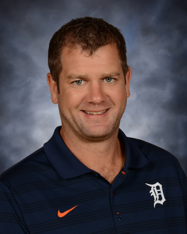 A smiling man with short brown hair wearing a dark blue polo shirt with an orange logo and a white letter 'D' on the left side.