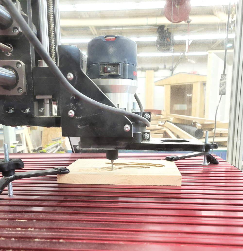 A close-up view of a woodworking router in operation, positioned above a wooden workpiece on a red work surface.