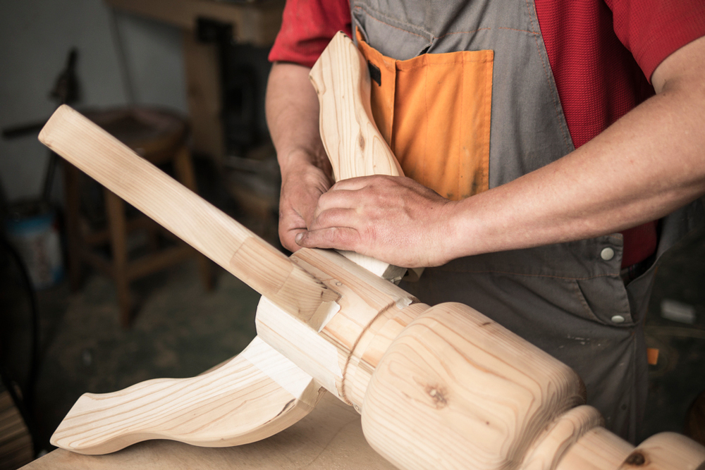 A craftsman is assembling a wooden piece, focusing on the intricate details of the joinery, with hands positioned carefully on the wood.