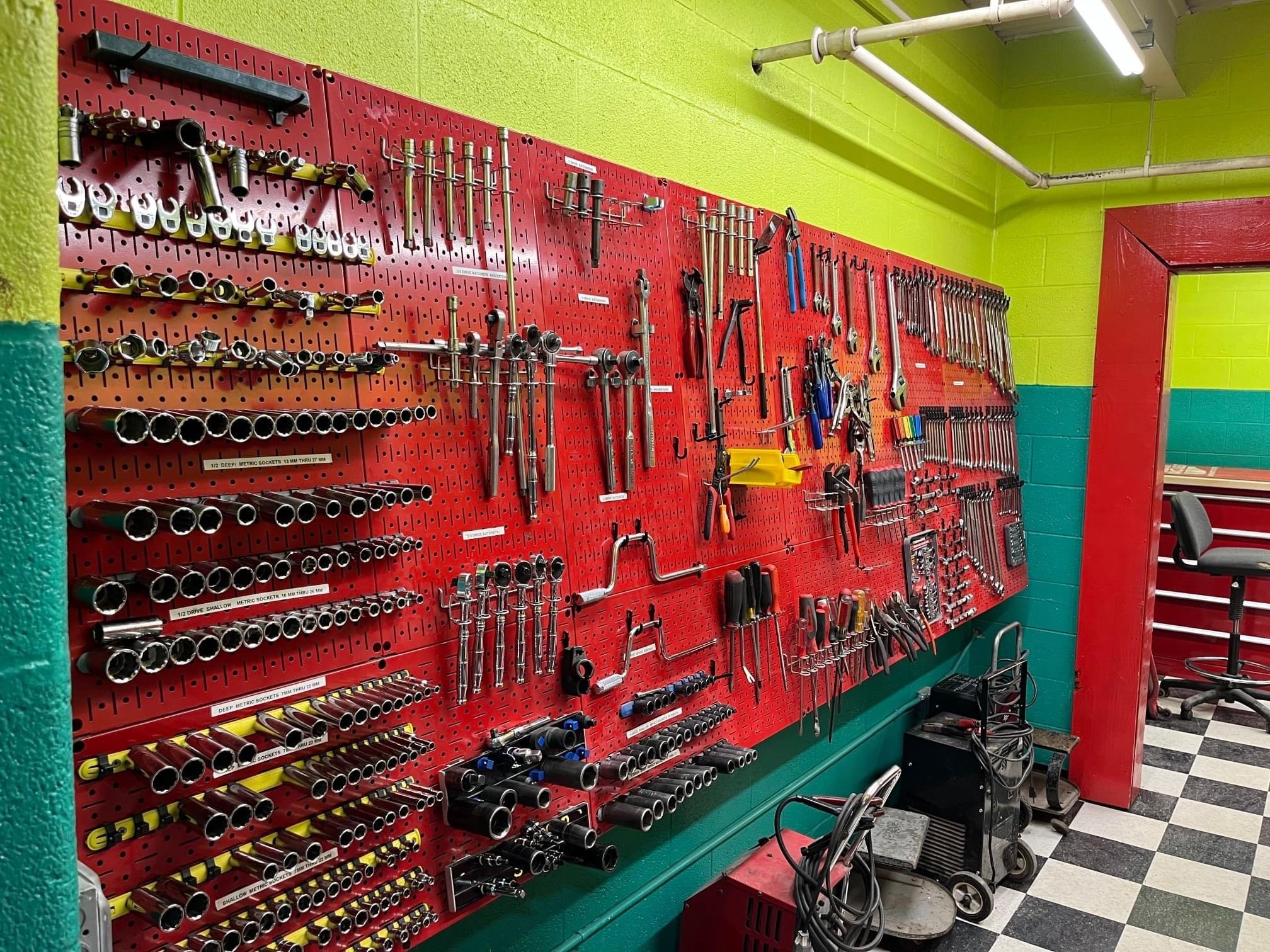 A wall-mounted tool organizer displaying a variety of hand tools, including wrenches, sockets, and pliers, against a brightly colored background.