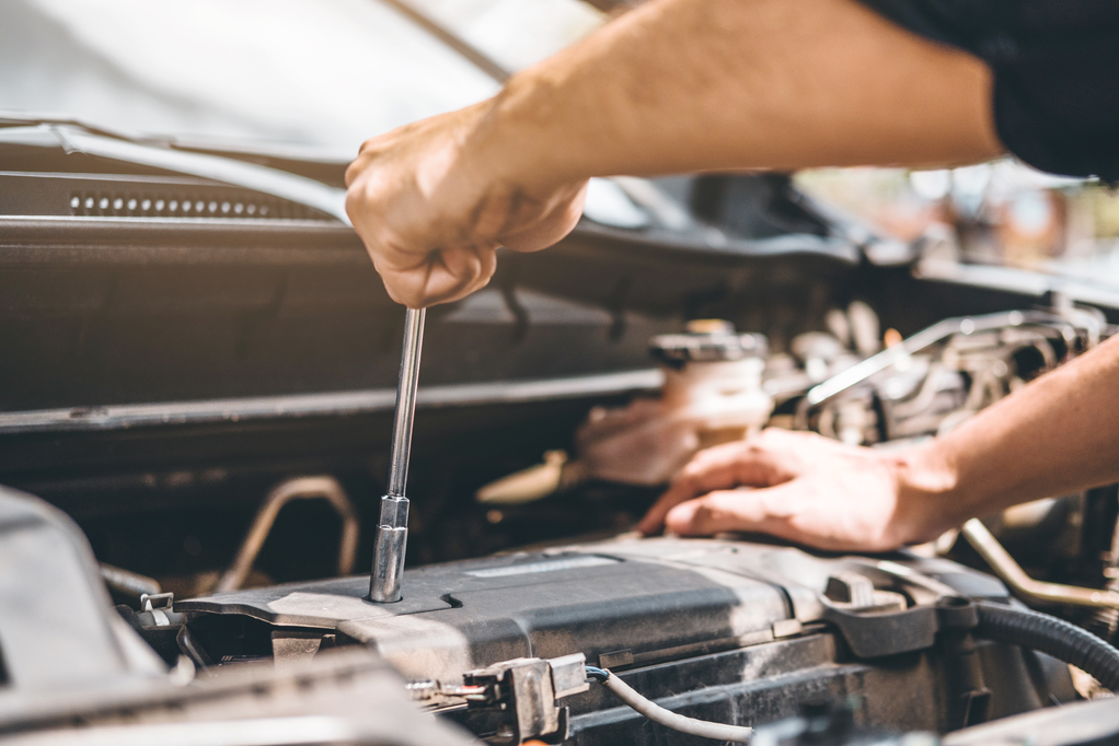 A mechanic uses a wrench to work on the engine of a car, with a focus on the hands and tools involved in the repair process.