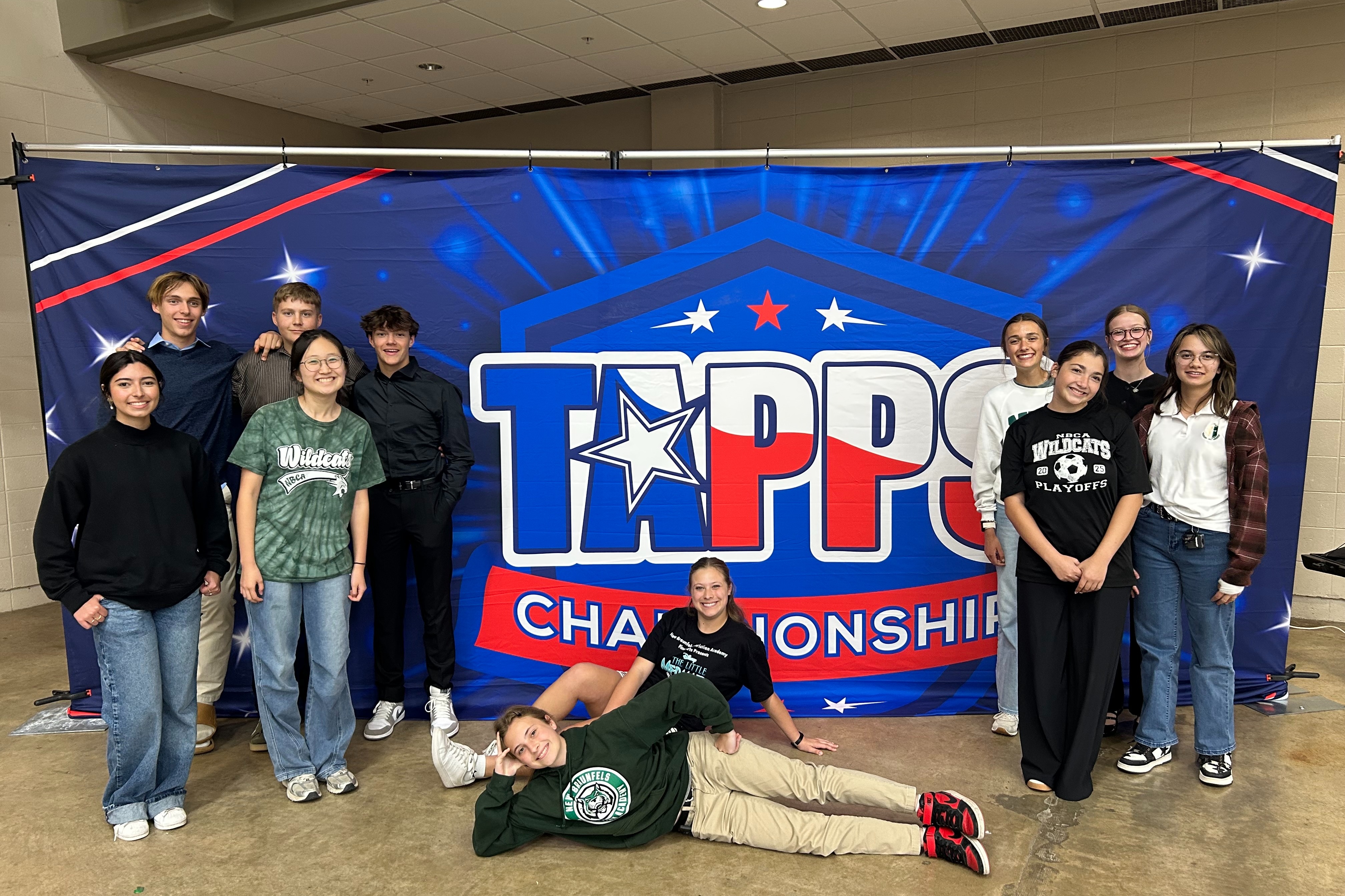 Students pose for a group photo in front of a banner with text reading "TAPPS Championship".