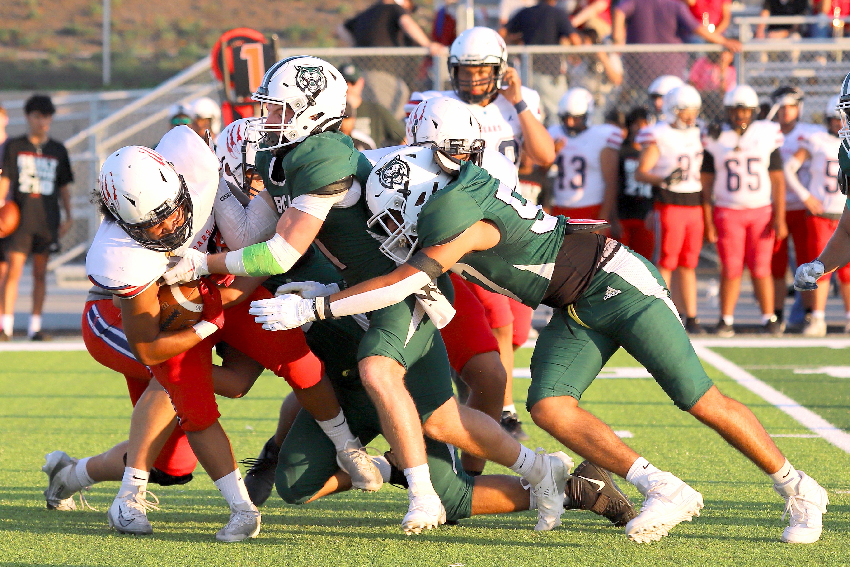 Several players in football uniforms tackle each other on a field. One player holds a ball.