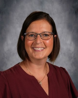 A woman wearing a green shirt smiles brightly at the camera, exuding warmth and positivity.