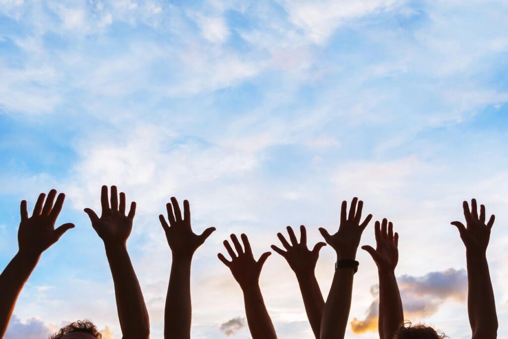 Hands raised towards a clear blue sky, symbolizing joy and freedom against a serene backdrop.