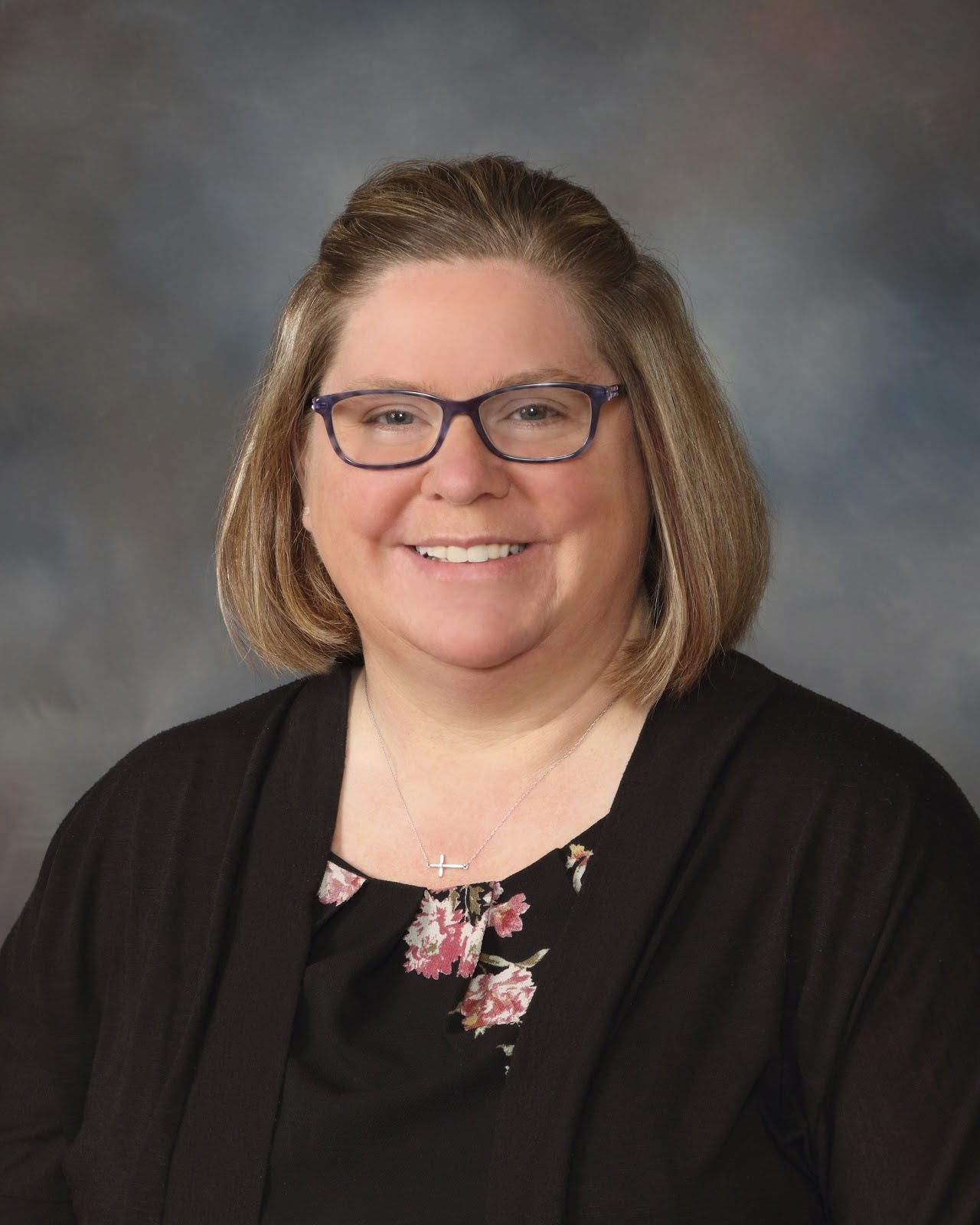 A woman wearing glasses and a black shirt, looking confidently at the camera with a neutral background.