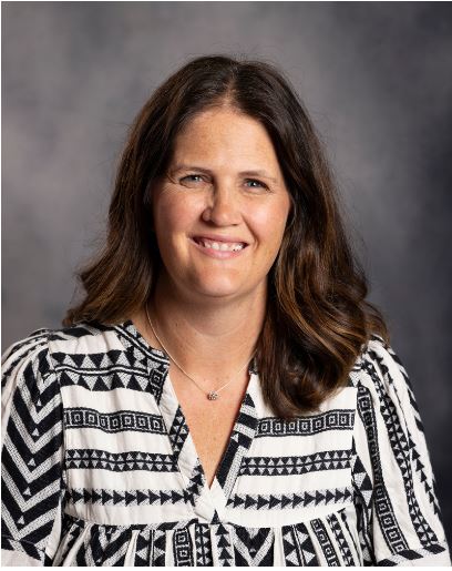 A woman wearing a black and white shirt smiles warmly, exuding joy and positivity in her expression.