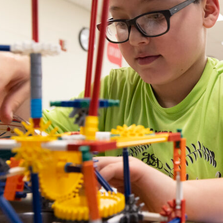A boy wearing glasses is focused on assembling a colorful toy, showcasing his concentration and creativity.