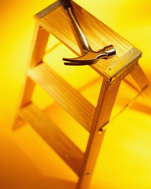  A wooden ladder positioned alongside a hammer and a screwdriver, showcasing tools for construction or repair tasks.