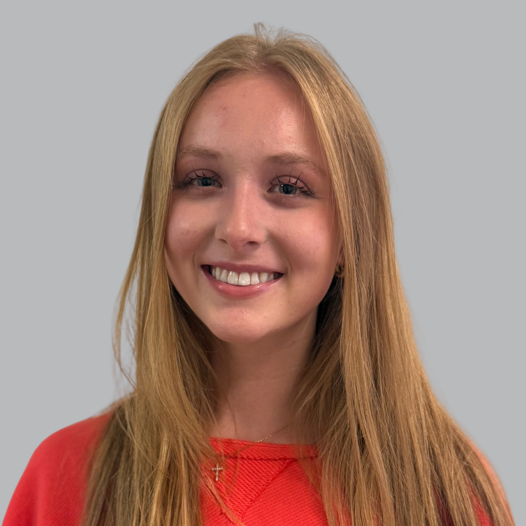 A woman with long blonde hair smiles against a plain gray background, wearing a red long-sleeved shirt.