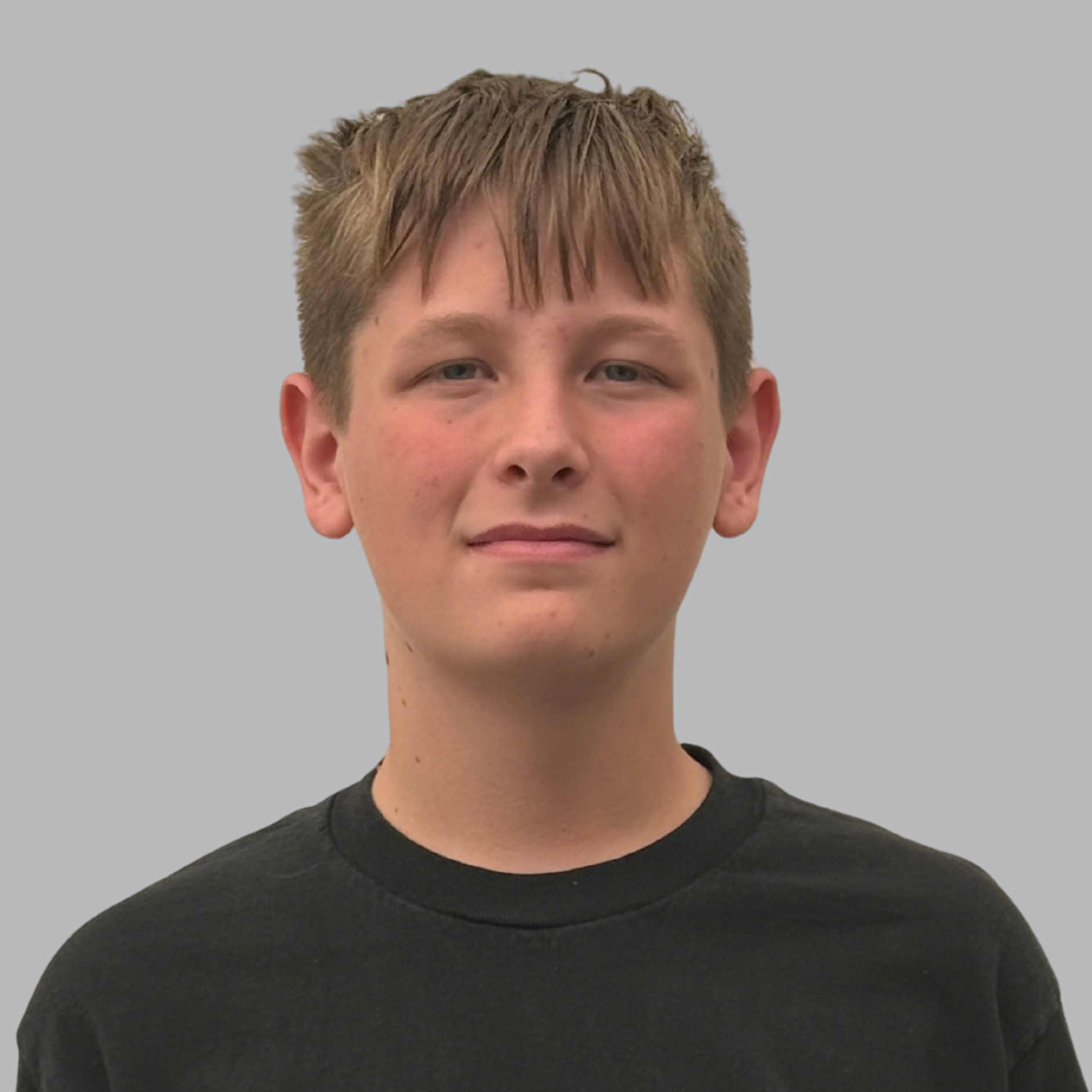 A boy with short blond hair, wearing a black T-shirt with a white logo, looks directly into the camera.