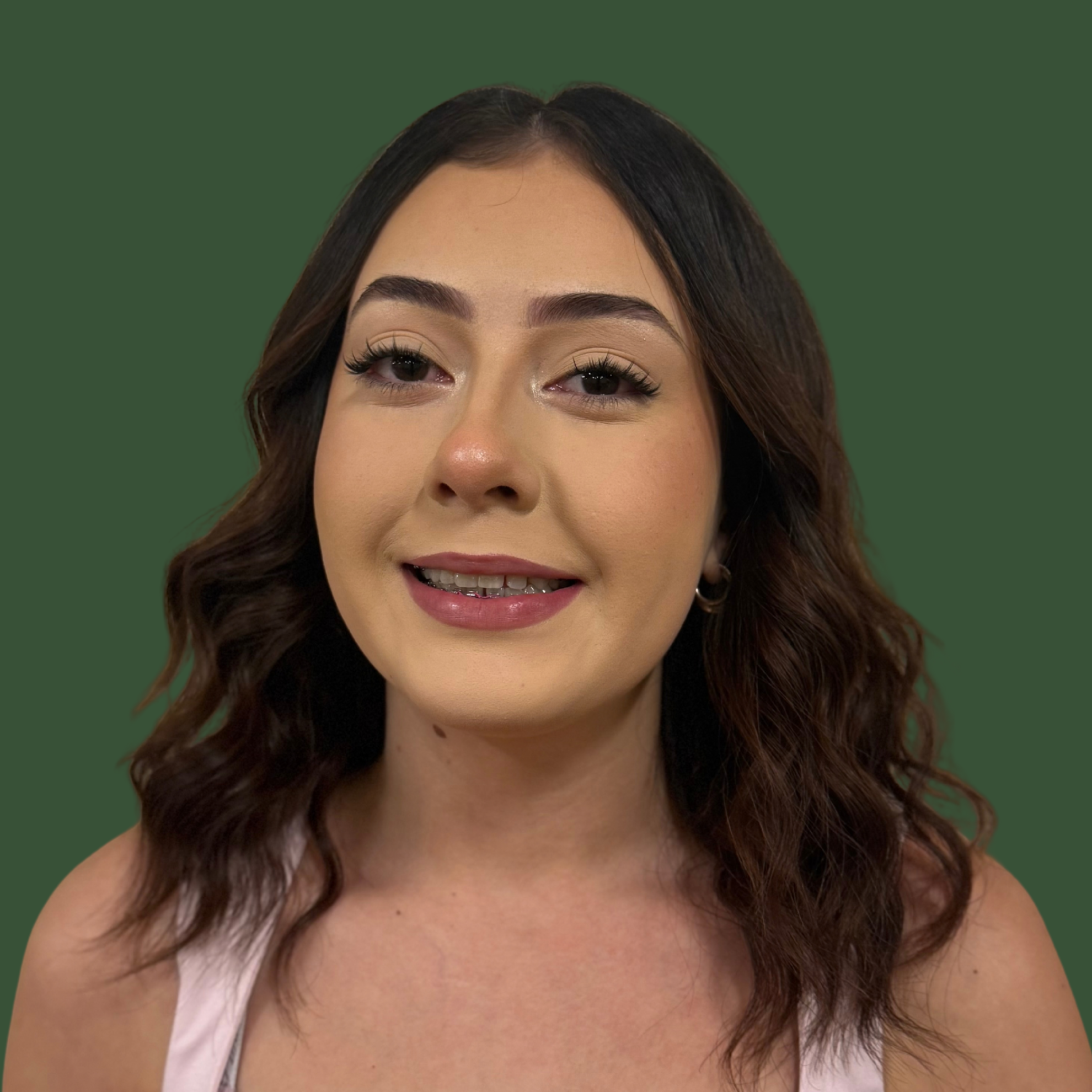 Woman with dark curly hair wearing pink top, smiling. Green background.