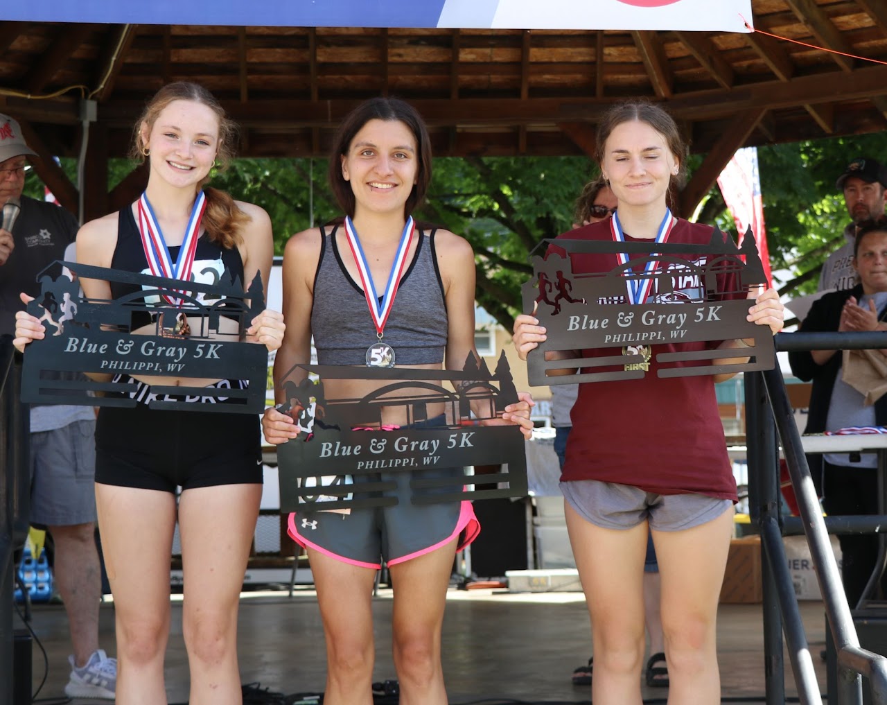 Three female runners proudly display their awards from the Blue & Gray 5K event, adorned with medals around their necks.