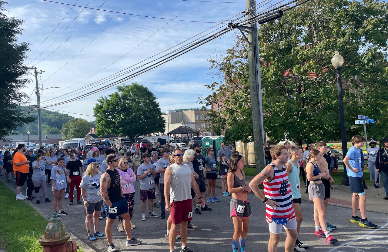 A large group of runners in various athletic gear, gathered on a street, preparing for a race under a clear blue sky.