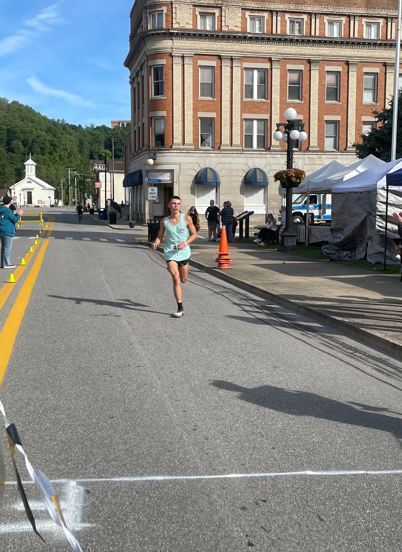 A runner sprints towards the finish line in a vibrant town, with spectators and a historic building in the background.
